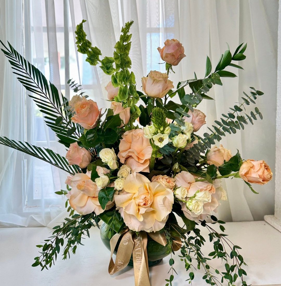 A grand arrangement of peach roses, bells of Ireland and palm leaves